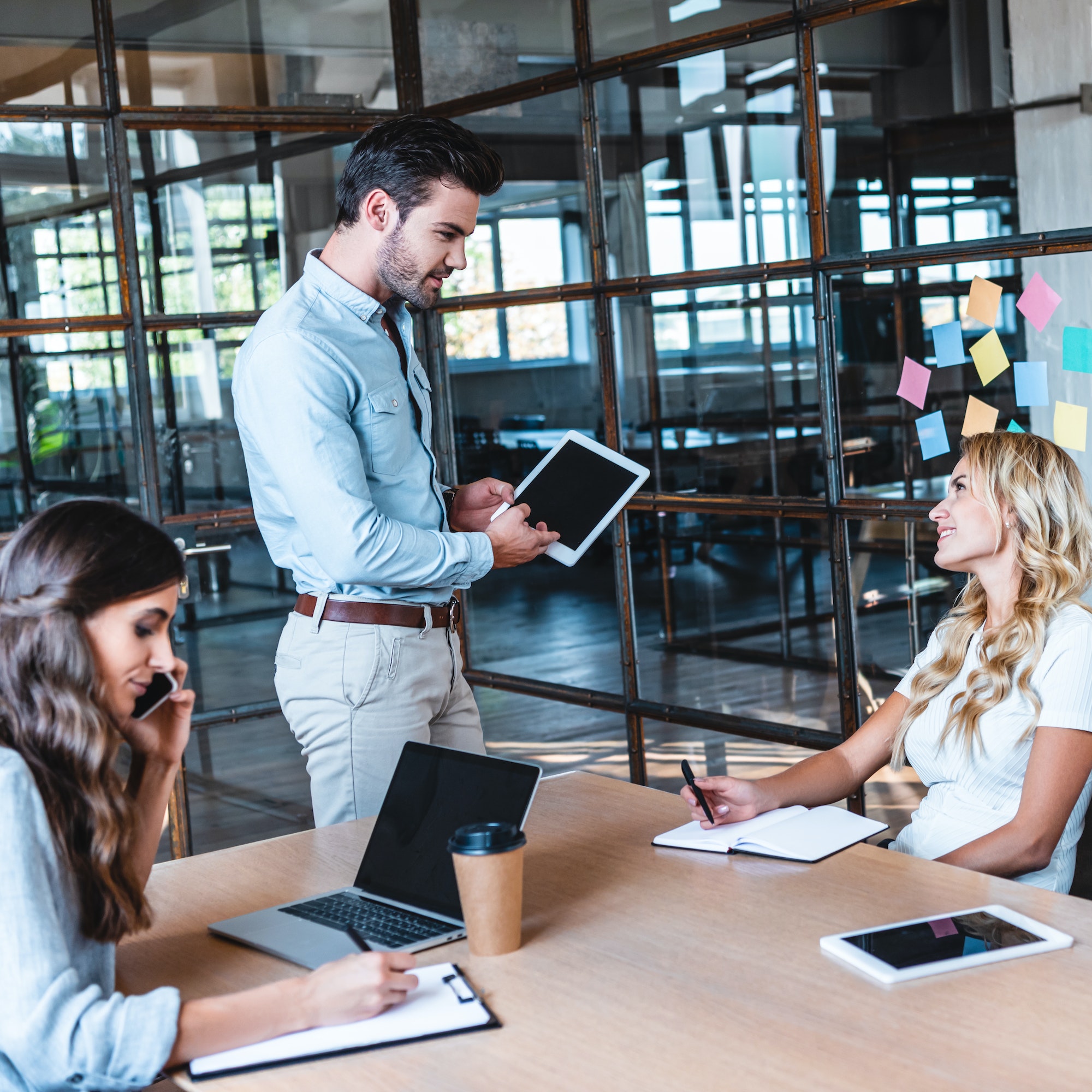 young businessman using digital tablet and looking at smiling female colleague at workplace